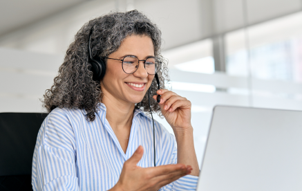 A professional woman with glasses and a headset engaged in a conversation on her laptop, discussing career opportunities in government solutions.